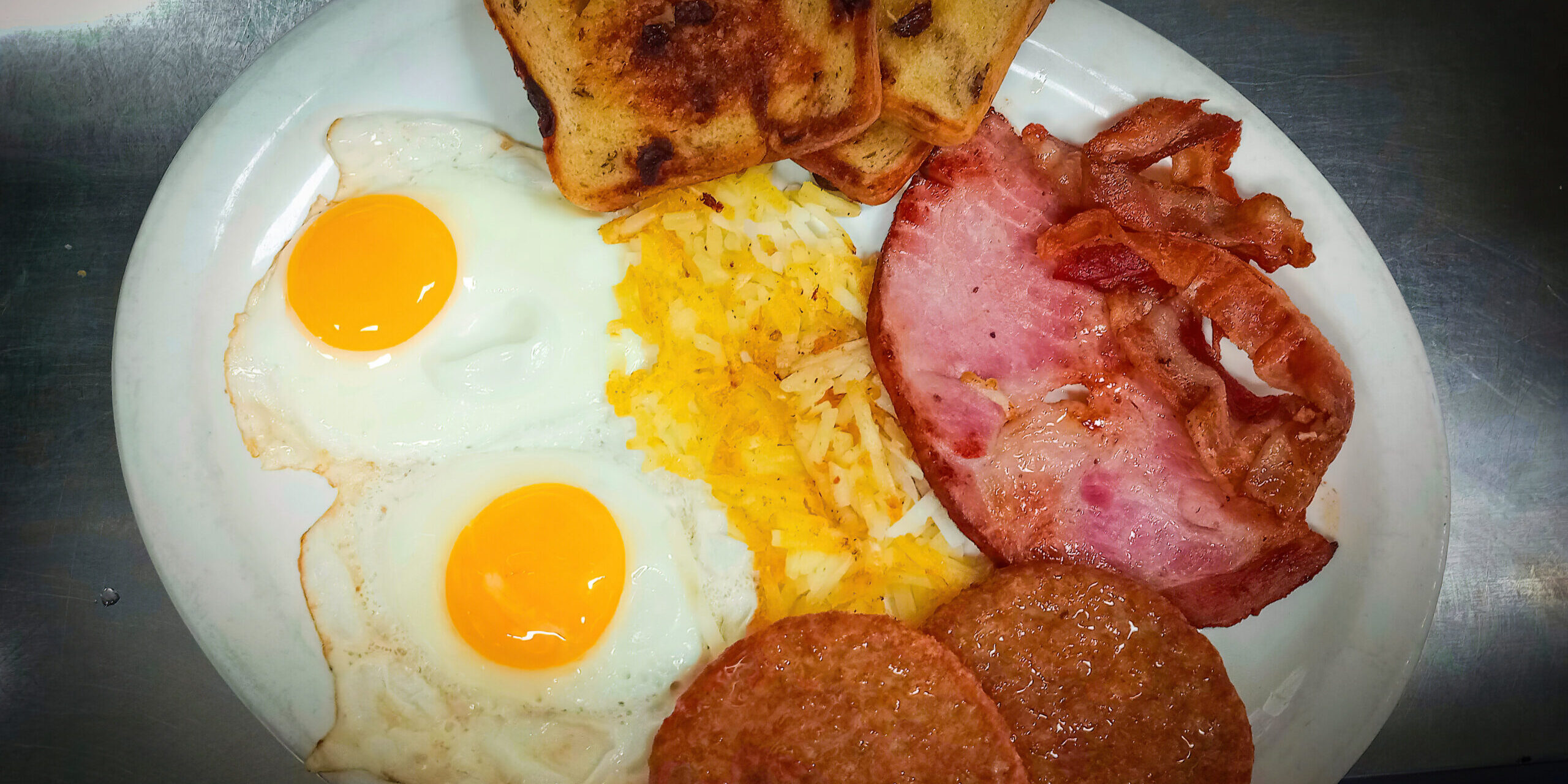 belly busters breakfast including two sausage patties, a slice of ham, two slices of bacon, hash browns, two fried eggs and a side of raisin toast