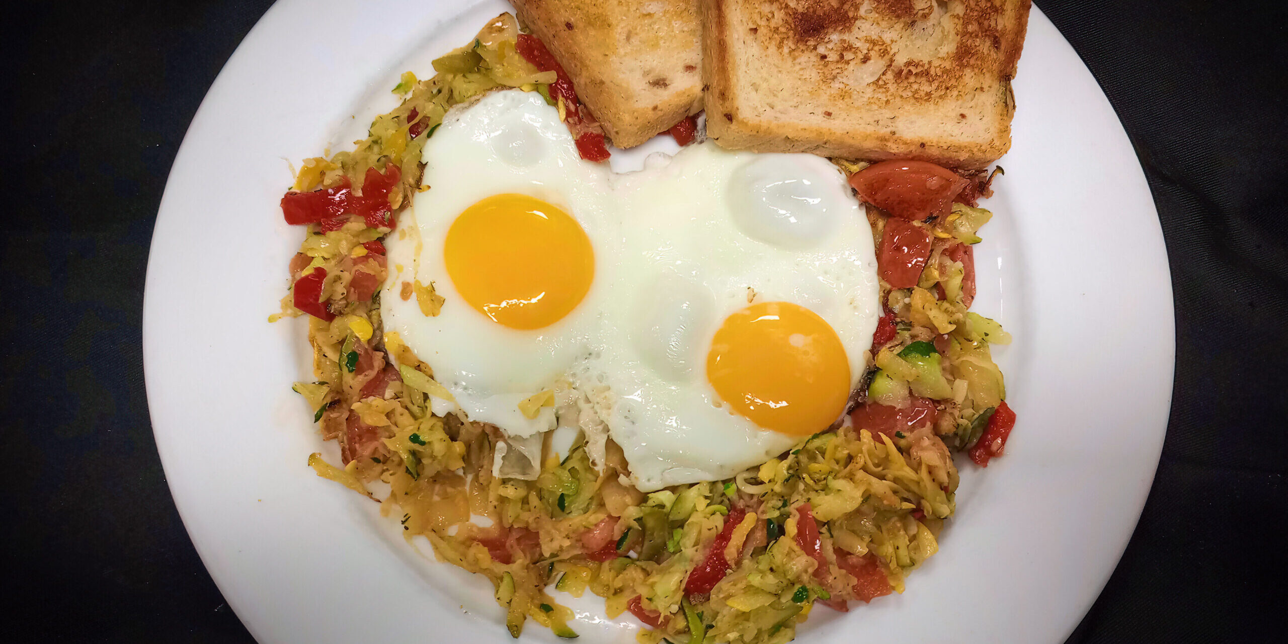 veggi hash topped with fried eggs and a side of toast